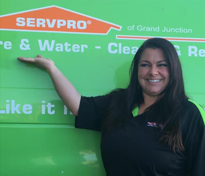 woman in SERVPRO shirt in front of SERVPRO truck pointing to SERVPRO logo